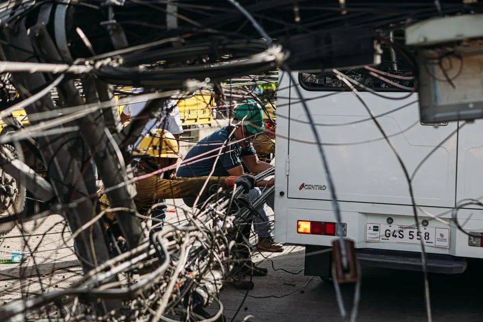 Technicians working on tangled overhead wires next to a vehicle on a sunny day.